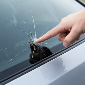 Une main pointe une fissure sur un pare-brise, illustrant comment faire jouer assurance bris de glace.