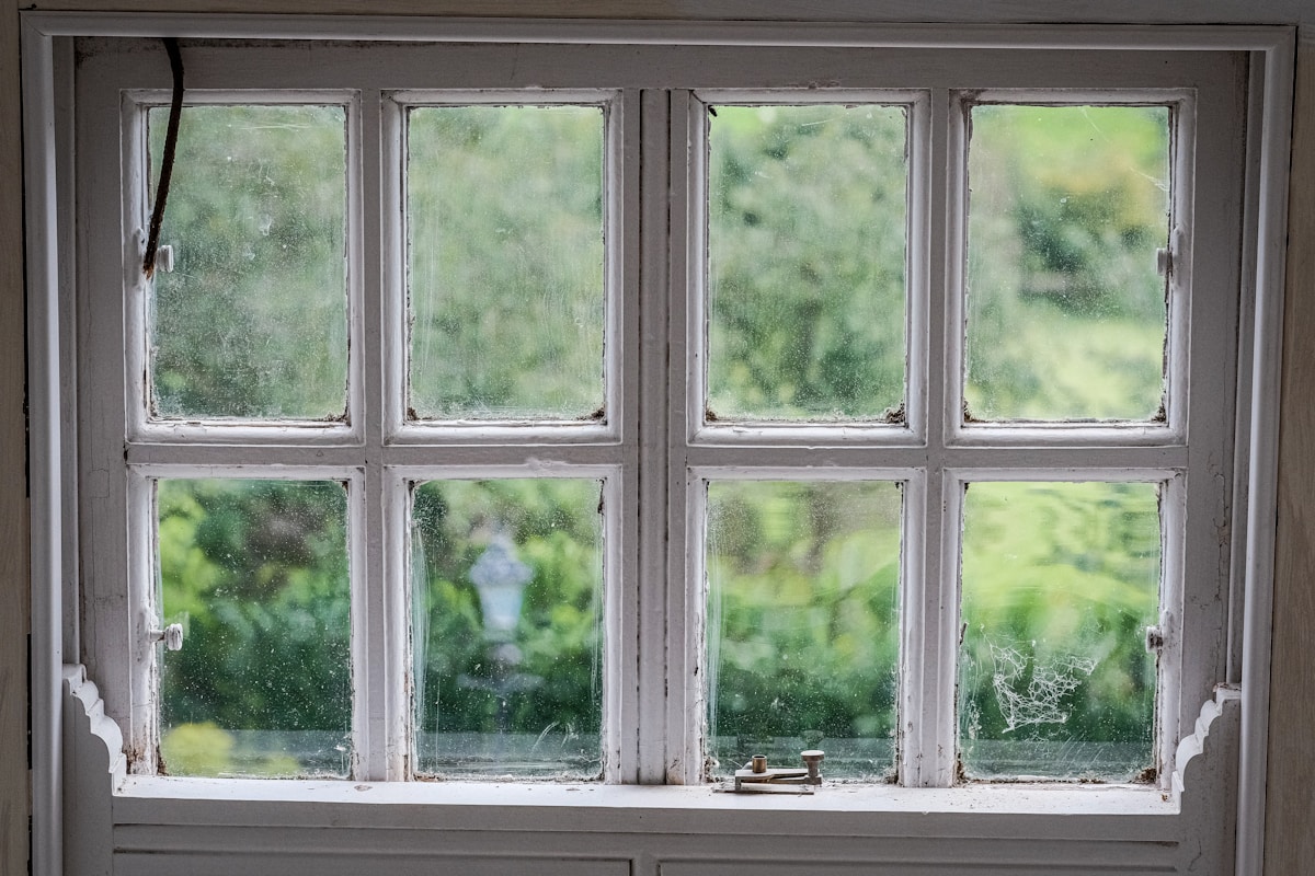 Fenêtre ancienne avec cadre en bois, vue sur un jardin verdoyant.