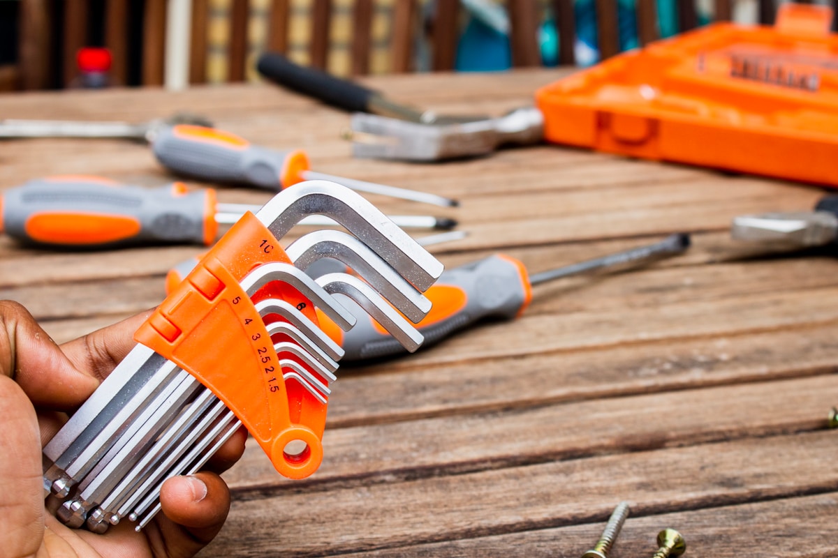 Ensemble d'outils de bricolage orange et gris sur un plan de travail en bois.