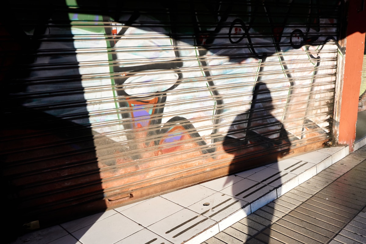 Rideau métallique avec graffitis colorés et ombre d'une personne.