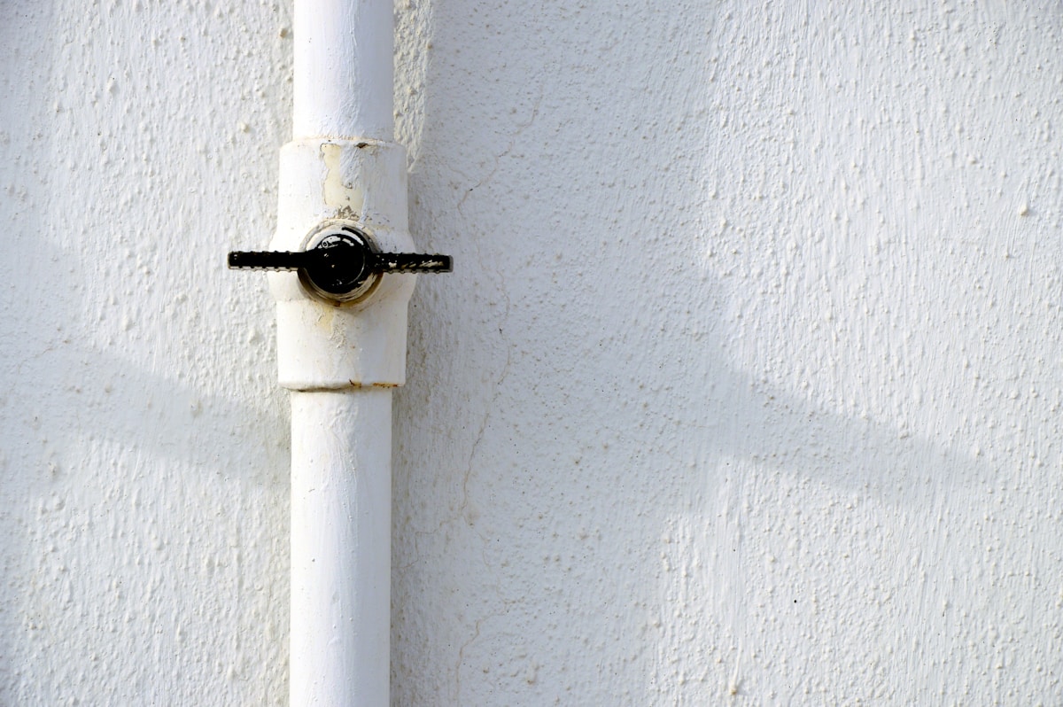 Tuyau blanc avec valve noire sur mur blanc texturé.