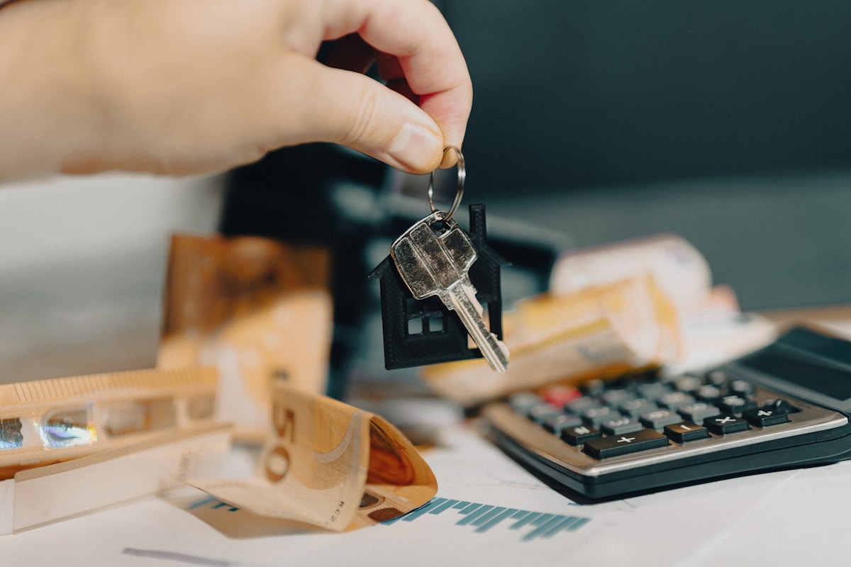 Clé de maison sur un bureau avec calculatrice et documents.