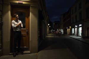 Homme en costume debout dans l'embrasure d'une porte, rue sombre la nuit.
